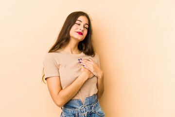 Young caucasian woman isolated en beige background has friendly expression, pressing palm to chest. Love concept.