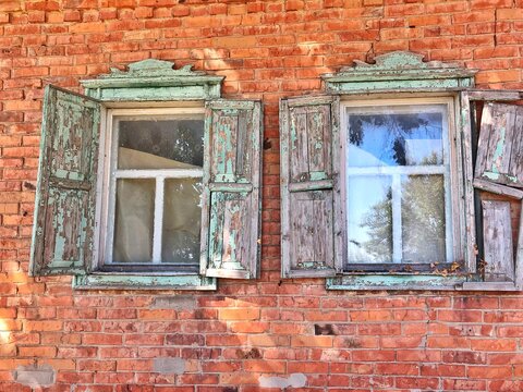 Dilapidated house with wooden shutters. Open wooden shutters with peeled paint