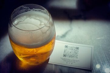 Selective focus on a fresh glass of beer with a QR code for the online menu. Summer 2020. New normal.