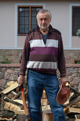 Elderly man with ax stands in front of pile of firewood