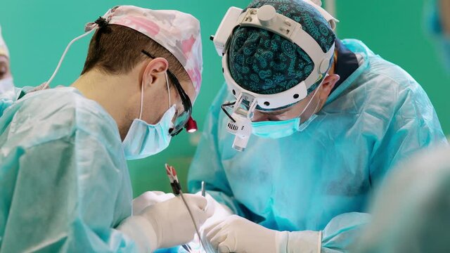 Group of medical specialists during surgery. Professional doctors in medical masks and caps work with surgical equipment. Health care concept.