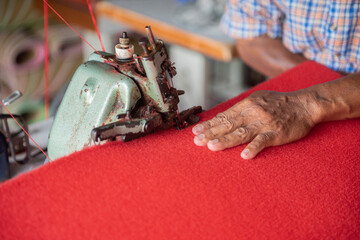 Close up hand of old man sewing a red rug