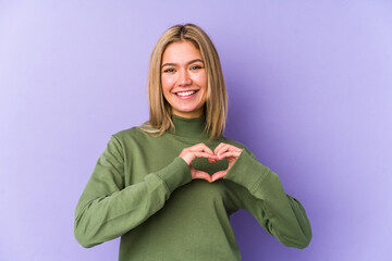 Young blonde caucasian woman isolated smiling and showing a heart shape with hands.