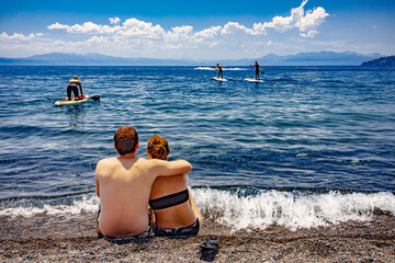 young couple watch kayakers from the beach
