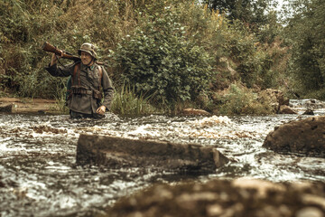 A military reenactor from the second world war, in the form of the Finnish army, crosses a stormy river