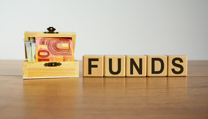 Concept word 'funds' on cubes on a beautiful wooden table, small chest with euro bills. Beautiful white background. Business concept. Copy space.