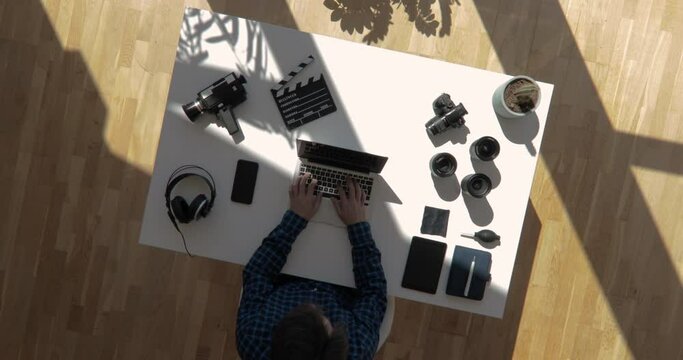 Spinning top view shot of film maker sitting on desk writing on a laptop with floating sun shot in 4k