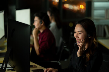 Asian customer service call center representative working in the night overtime office with computer monitor and headphone new normal social distancing work from home virus pandemic