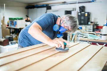 Middle-aged artist with dust mask sanding wood in his home studio.Handmade concept