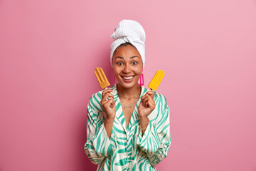Good looking healthy young woman holds two popsicles on sticks, has happy mood, wears casual...