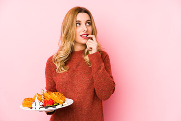 Young blonde woman eating a waffle dessert isolated relaxed thinking about something looking at a copy space.