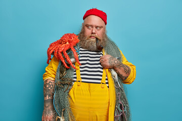 Male mariner looks with scared expression at octopus, afraids big sea creature, poses with fishing...