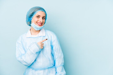 Young surgeon woman isolated smiling and pointing aside, showing something at blank space.