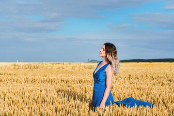 Beautiful woman in a blue dress in a wheat field against the sky. The concept of freedom and naturalness