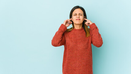 Young woman isolated on blue background covering ears with fingers, stressed and desperate by a...