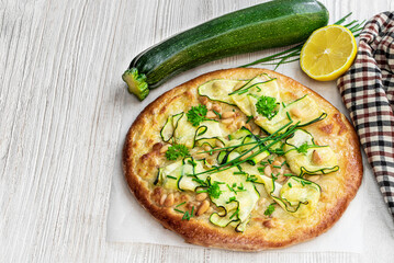 Vegetarian pizza with zucchini and pine nuts on white wooden table