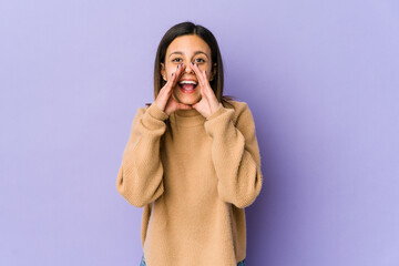 Young woman isolated on purple background saying a gossip, pointing to side reporting something.