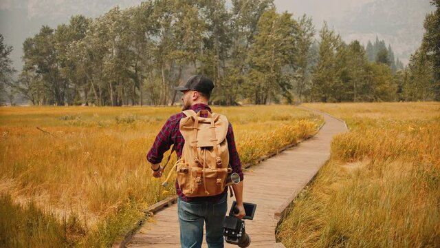 Photographer with professional camera set walking through autumn Yosemite National Park, holding camera set and looking around