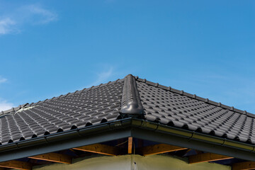 The roof of a single-family house covered with a new ceramic tile in anthracite against the blue sky, visible ridge tile.