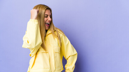 Young blonde woman isolated on purple background celebrating a victory, passion and enthusiasm, happy expression.