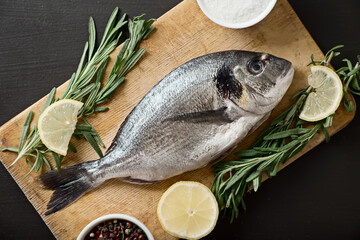 Raw dorado with lemon, pepper and rosemary on a board, top view.