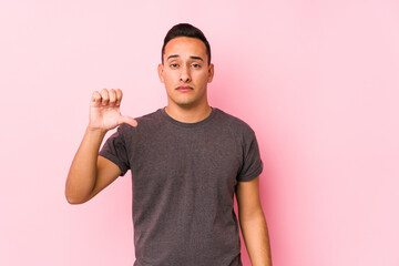 Yooung latin man posing in a pink backgroundshowing a dislike gesture, thumbs down. Disagreement...