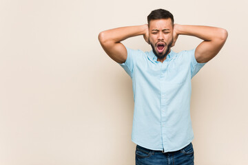 Young south-asian man covering ears with hands trying not to hear too loud sound.