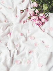 Fototapeta na wymiar Pink roses and petals on crumpled white fabric. Natural elegant decoration. Romantic background. Top view, flat lay.