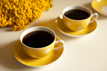 Two yellow coffee cups on white background, coffee break and caffeine addiction concept. yellow flowers on the table