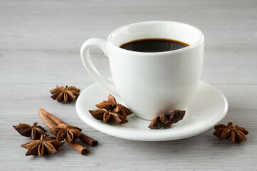 A cup of aromatic black coffee in a white cup on a wooden background with star anise and cinnamon sticks.
