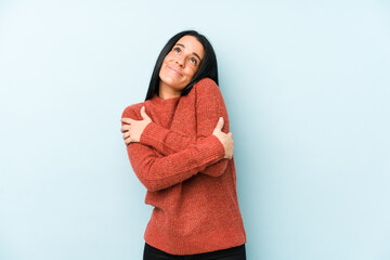 Young caucasian woman isolated on a blue background hugs, smiling carefree and happy.