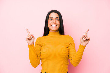Young caucasian woman isolated on a pink background indicates with both fore fingers up showing a...