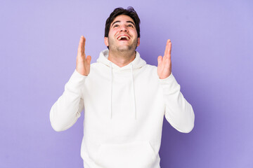 Young man isolated on purple background laughs out loudly keeping hand on chest.