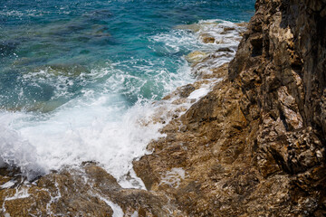 Wonderful views of the blue Mediterranean Sea. Sunny rocks, waves with foam and splashing water. The wave crashes into the rocks on the shore
