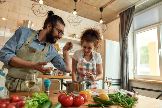 Italian man adding pepper, spice to the soup while woman stirring it and smiling. Couple preparing a meal together in the kitchen. Cooking at home, Italian cuisine