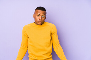 Fototapeta premium Young latin man isolated on purple background shrugs shoulders and open eyes confused.