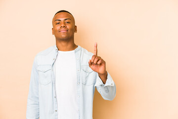 Young latin man isolated on beige background showing number one with finger.