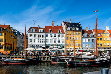 Fototapeta na wymiar Scenic summer view of the must-see Nyhavn pier in Copenhagen, with people having relax, colorful buildings and boats.