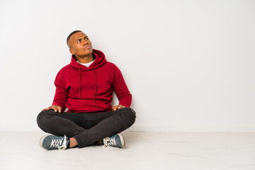 Young latin man sitting on the floor isolated dreaming of achieving goals and purposes