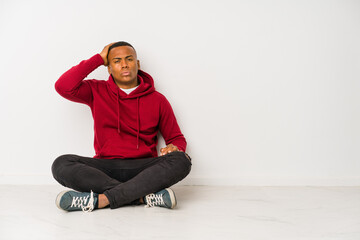 Young latin man sitting on the floor isolated tired and very sleepy keeping hand on head.