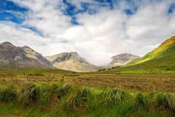 Fototapeta premium Beautiful mountains in Connemara, county Galway, Ireland; Warm sunny day, Clouds over peaks, Vast green fields.