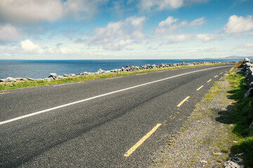 Small asphalt road by Atlantic ocean, Burren National geo park, Ireland. Nobody, Warm sunny day. Beautiful cloudy blue sky. Part of Wild Atlantic Way.