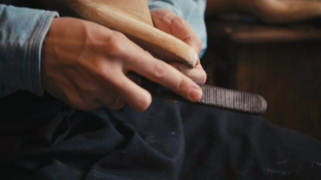 Close up shoemaker polishes wooden mold for shoes in workshop, man making leather boots, craft industry handmade