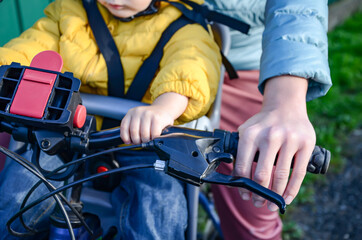 Fototapeta na wymiar Hands of mother and child on the handlebars of a bicycle. Child in a child seat and wearing seat belts. Concept: cycling with children, parenting, safety.