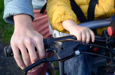 Hands of mother and child on the handlebars of a bicycle.