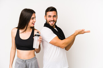 Young caucasian fitness couple isolated holding a copy space on a palm.