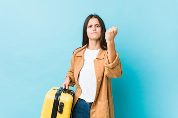 Young caucasian woman holding a suitcase showing fist to camera, aggressive facial expression.