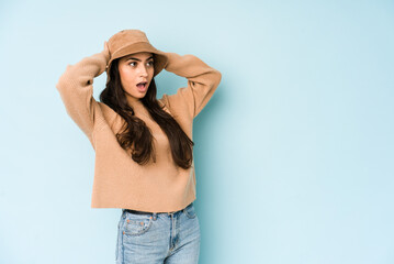 Naklejka premium Young indian woman wearing a hat isolated on blue background screaming, very excited, passionate, satisfied with something.