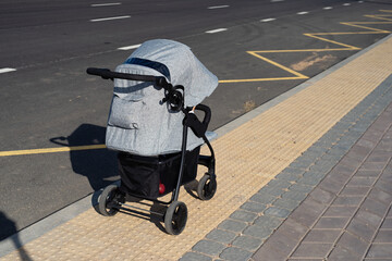 gray baby carriage stands on  troroir, baby legs are visible from carriage