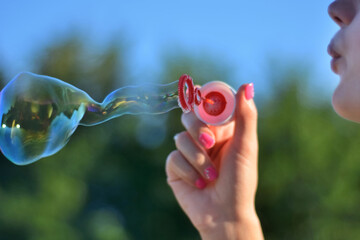Girl blowing soap bubbles outdoor in park on summer sunset. Happiness in nature concept. Close up,...